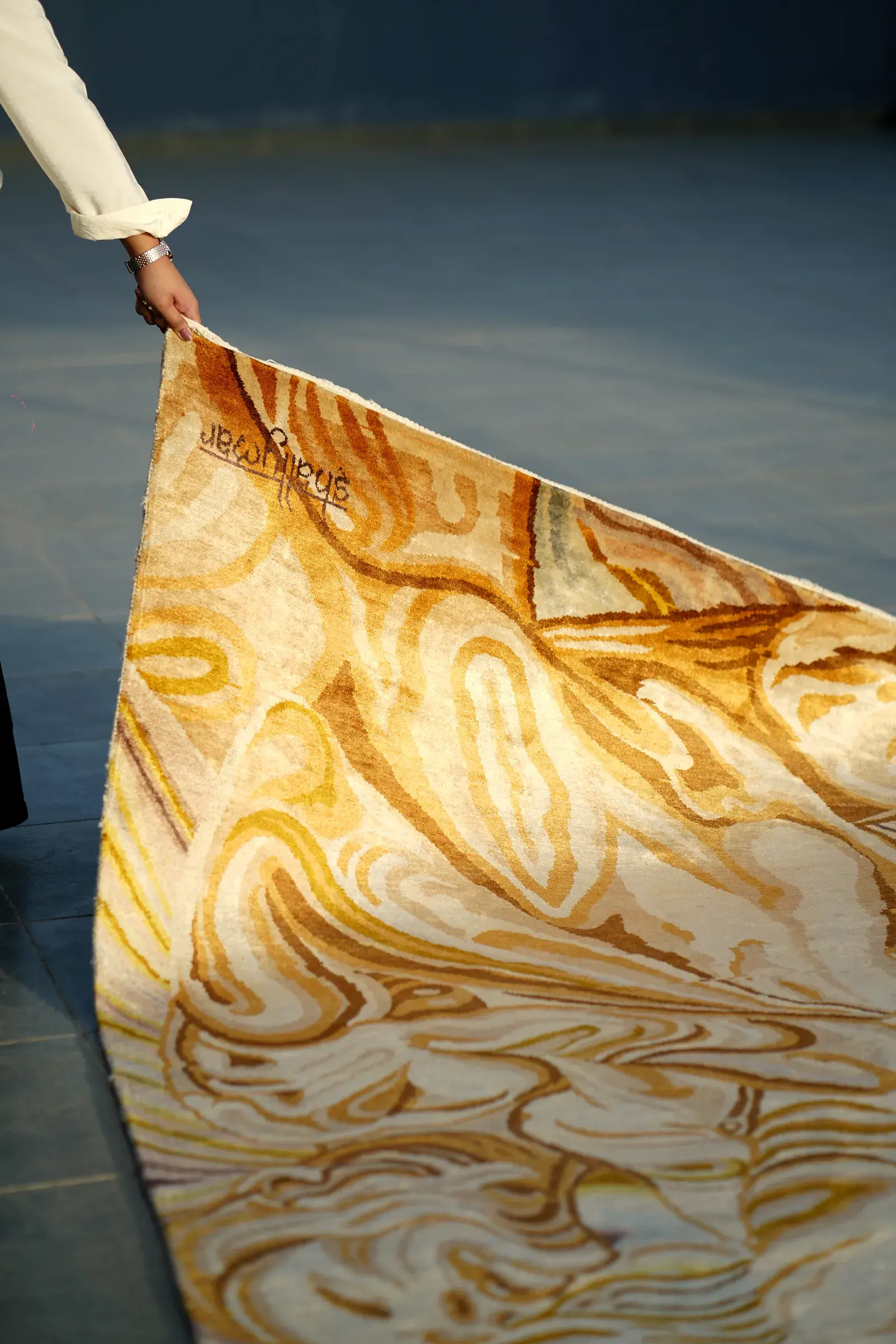 A hand lifting the corner of a gold silk rug