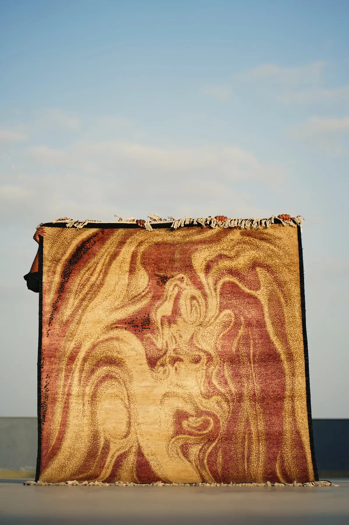 Alekhya, a Shallymar rug in rose and gold, held up against the evening sky